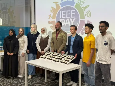 Students and faculty behind a tray of cupcakes in front of the IEEE Day banner