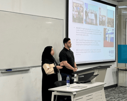Two presenters in front of slides about past branch competition results